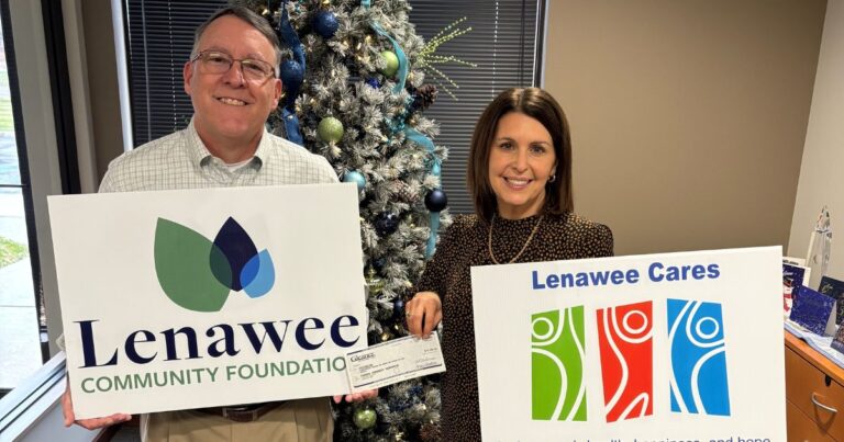 A check being presented with the recipient smiling, holding the check.